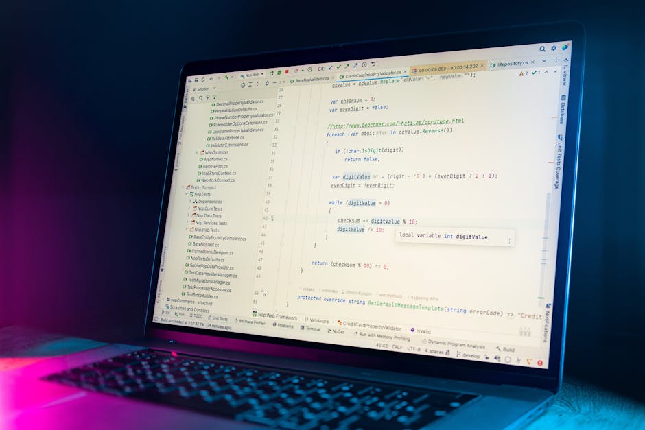 A close-up view of a laptop displaying a code editor with lines of programming code, set against a dark background illuminated by soft blue and pink lighting. The screen shows a detailed view of softw