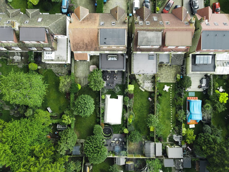 An aerial view of a residential neighborhood showing multiple back gardens side by side, each with distinct landscaping features. The gardens include lush green lawns with neatly trimmed grass, border