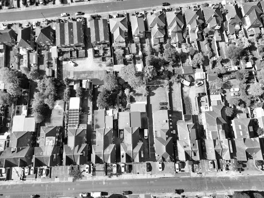 An aerial view of a residential neighborhood showing multiple back gardens side by side, each with distinct landscaping features. The gardens include lush green lawns with neatly trimmed grass, border